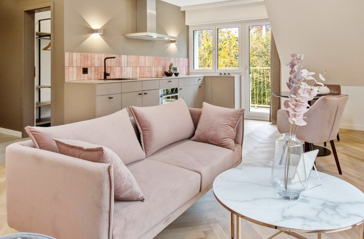 Offener Wohn- und Küchenbereich mit rosa Samtsofa, Marmor-Couchtisch und moderner Küchenzeile mit roséfarbenen Fliesenspiegel für Umbauten in Zürich. Offener Wohn- und Küchenbereich mit rosa Samtsofa, Marmor-Couchtisch und moderner Küchenzeile mit roséfarbenen Fliesenspiegel für Umbauten in Zürich.