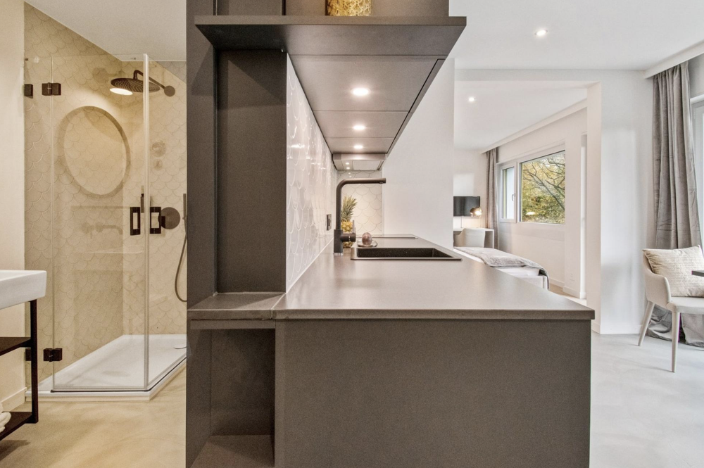 Modernisierter Wohnraum mit grossformatigen Bodenplatten, dunkler Design - Küchenzeile, Walk-In Dusche mit beigen Wandfliesen - Innenarchitektur mit Kontrastwirkung Modernisierter Wohnraum mit grossformatigen Bodenplatten, dunkler Design - Küchenzeile, Walk-In Dusche mit beigen Wandfliesen - Innenarchitektur mit Kontrastwirkung