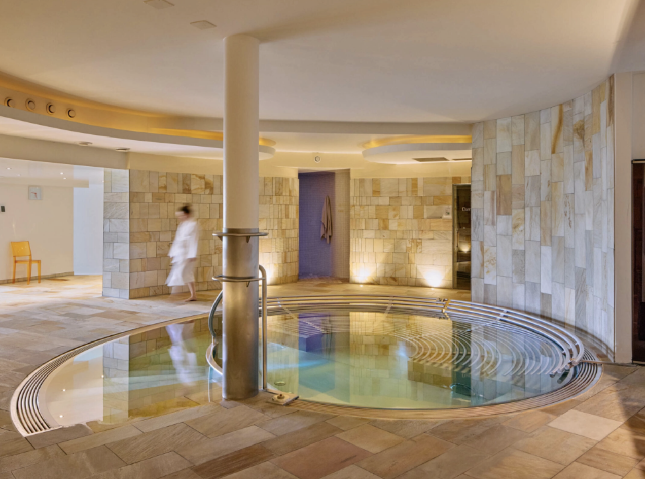 Hotel Stoos Wellnessbereich mit kreisförmiger Whirlpool, Wandverkleidung Naturstein und stimmungsvoller Lichtinszenierung - exklusiver Innenausbau für Spa und Badewelten. Hotel Stoos Wellnessbereich mit kreisförmiger Whirlpool, Wandverkleidung Naturstein und stimmungsvoller Lichtinszenierung - exklusiver Innenausbau für Spa und Badewelten.